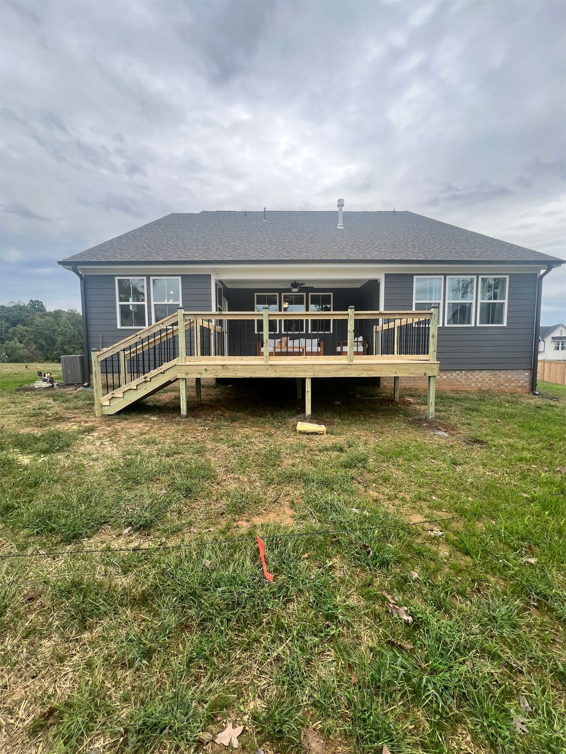 A new wooden deck attached to a gray house with black railings, in a grassy yard under a cloudy sky.