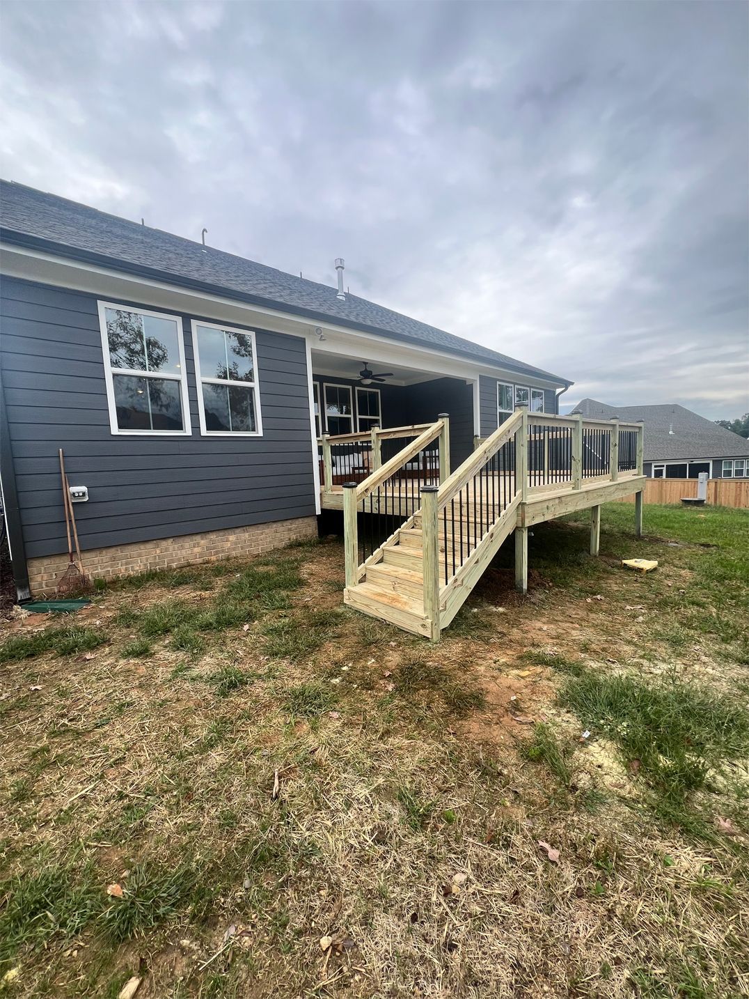 Wooden deck with stairs attached to a dark gray house, overlooking a grassy backyard.