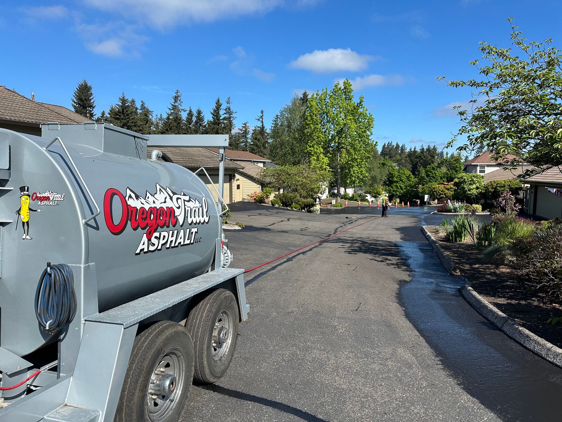 Paving crew truck on a residential street with fresh asphalt and a worker in the background