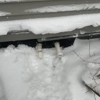 Snow-covered building's underside with two white drain pipes protruding.