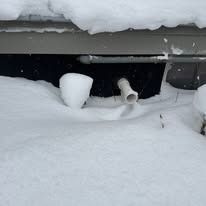 Snow covers a building, with a white drainage pipe visible.