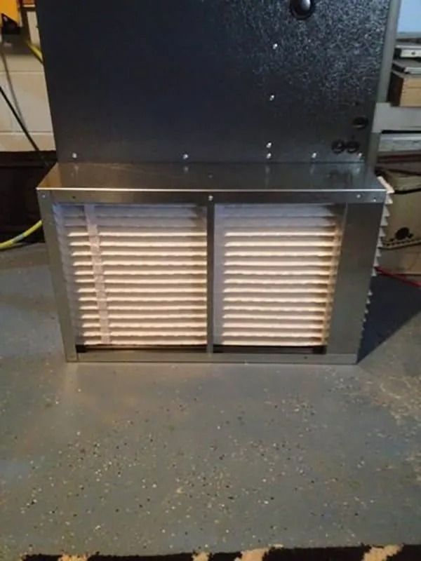 Furnace with two air filters, in a metal frame, set on a gray floor.