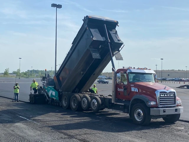 a dump truck is being loaded with asphalt in a parking lot