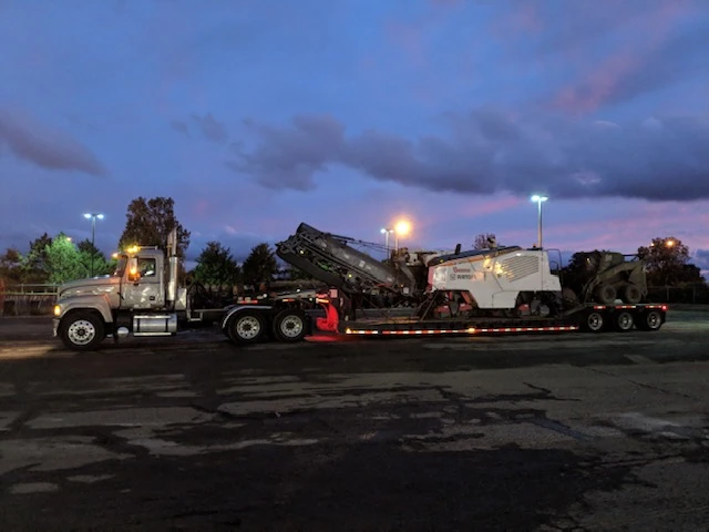 a truck is carrying a machine on a trailer in a parking lot at night 