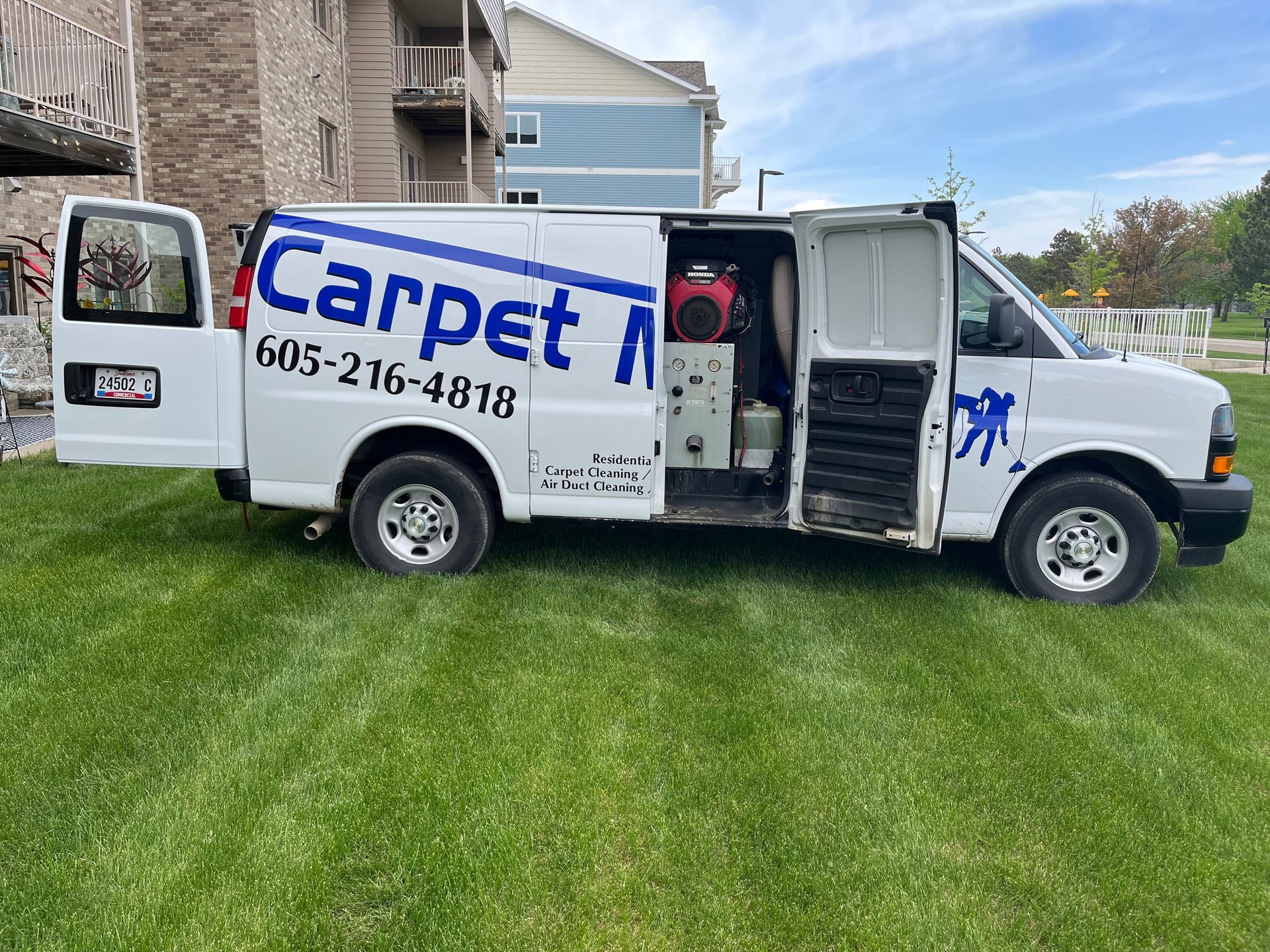 A white van with the door open is parked in a grassy field.