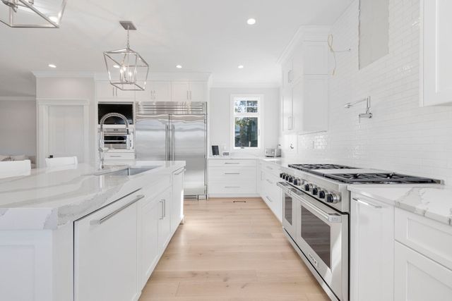 Bright white modern kitchen with island, stainless steel appliances, and wood floors