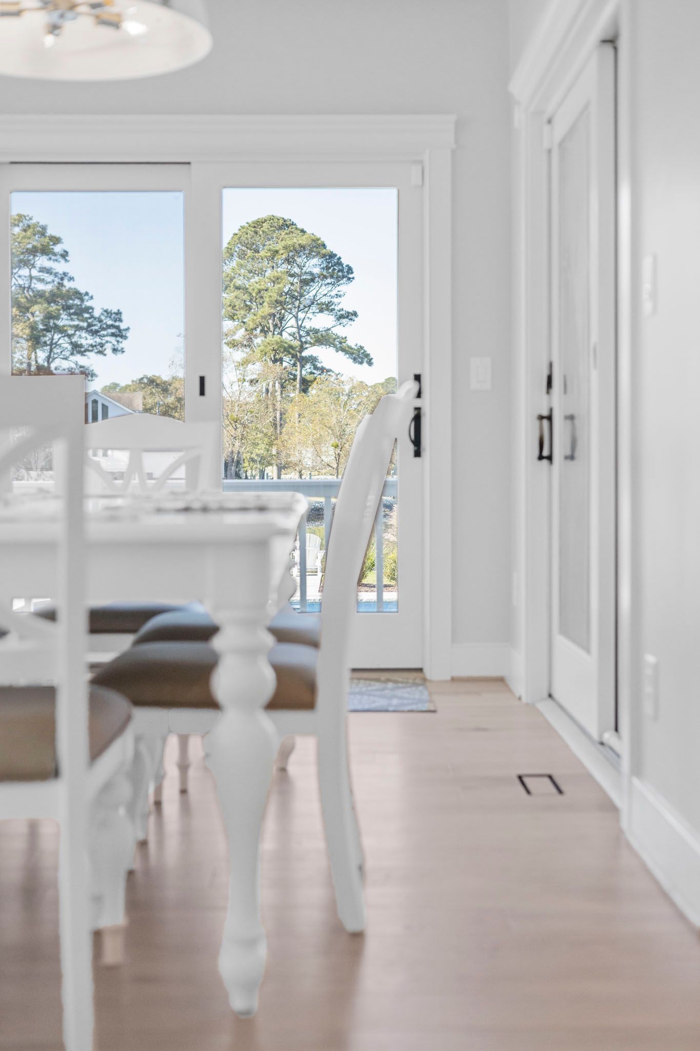 Bright dining room with white furniture, light wood floors, and glass doors opening to a patio.