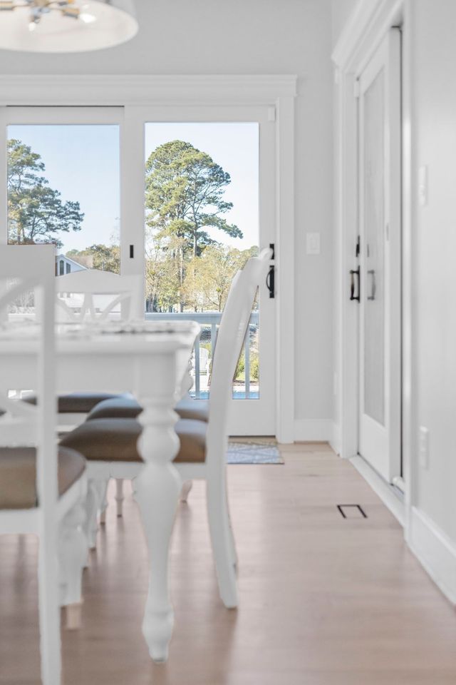 Bright dining room with white furniture, light wood floors, and glass doors opening to a patio.