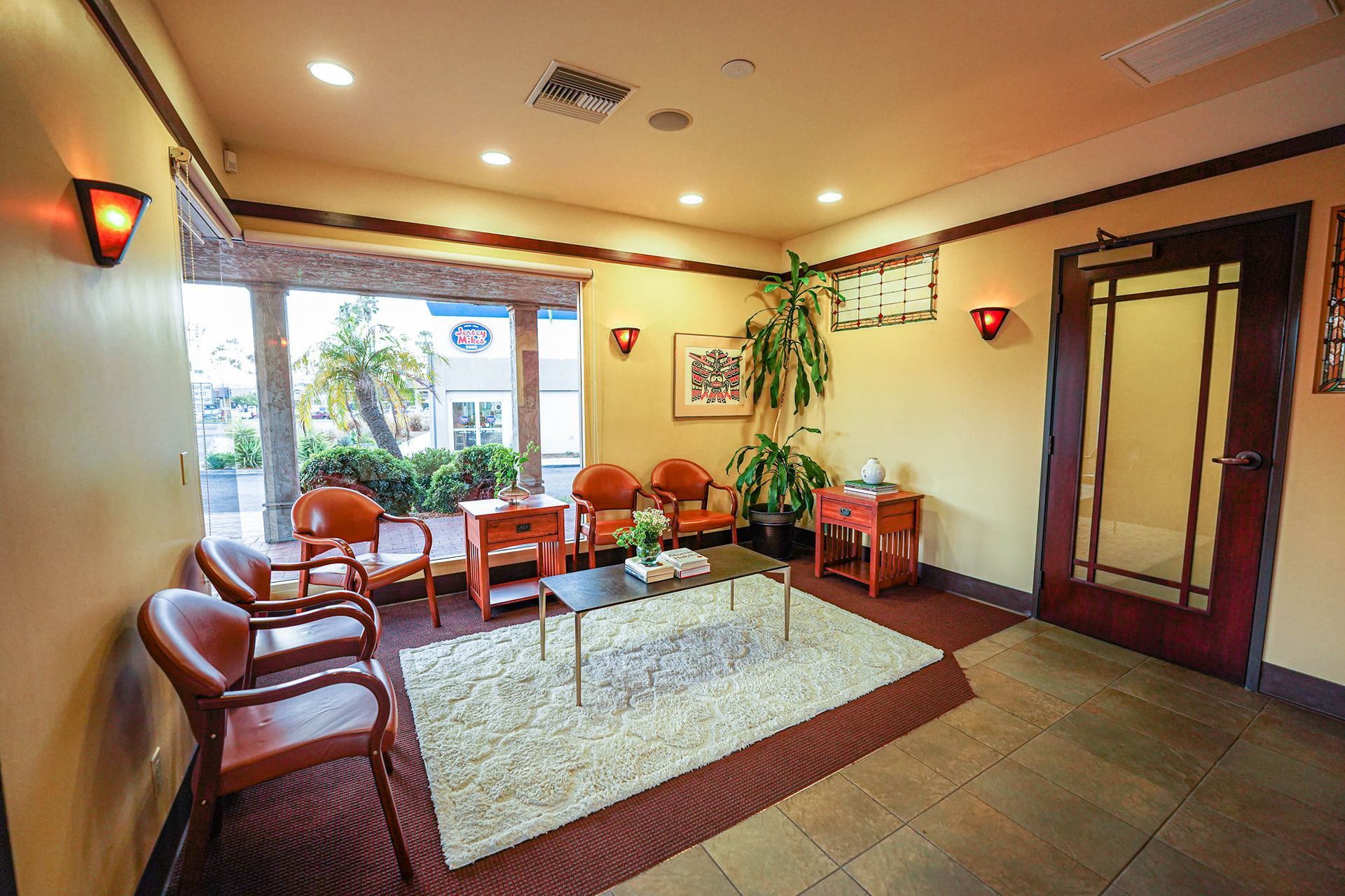 Waiting room with leather chairs, a rug, and small tables. Large window with outdoor view.