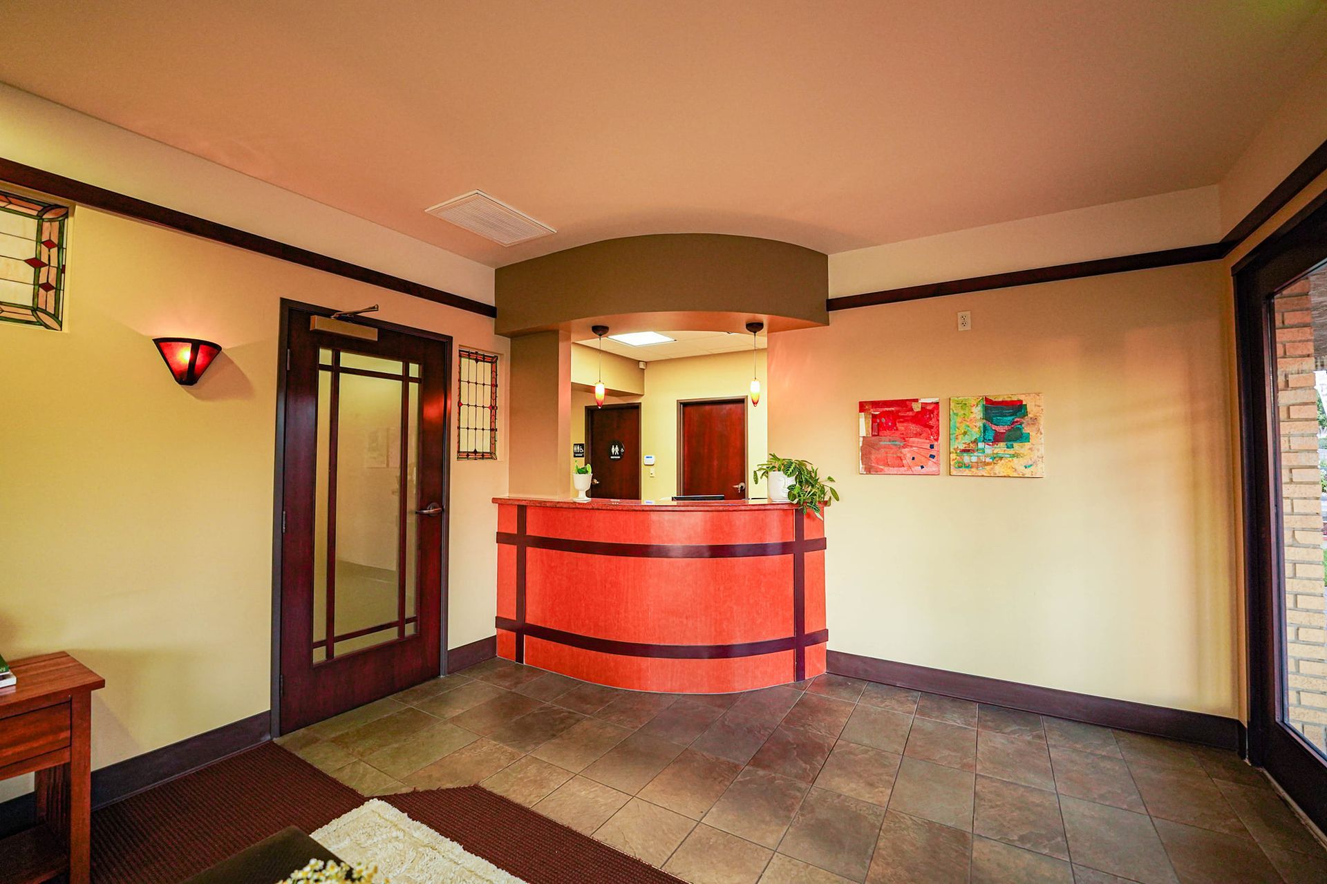 A reception area with an orange desk, brown trim, a glass door, and artwork.