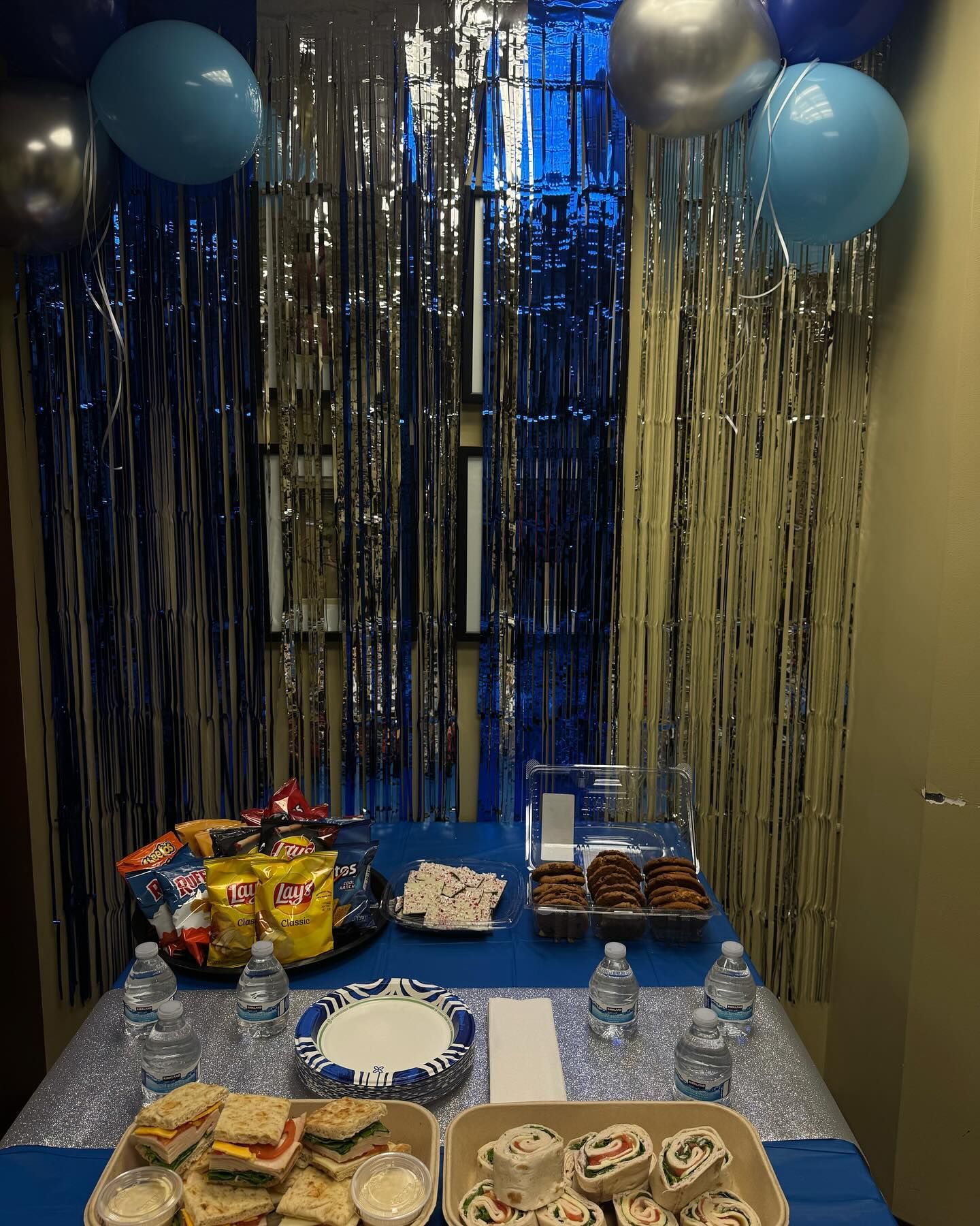 Party table with blue and silver decor, balloons, snacks, and drinks.