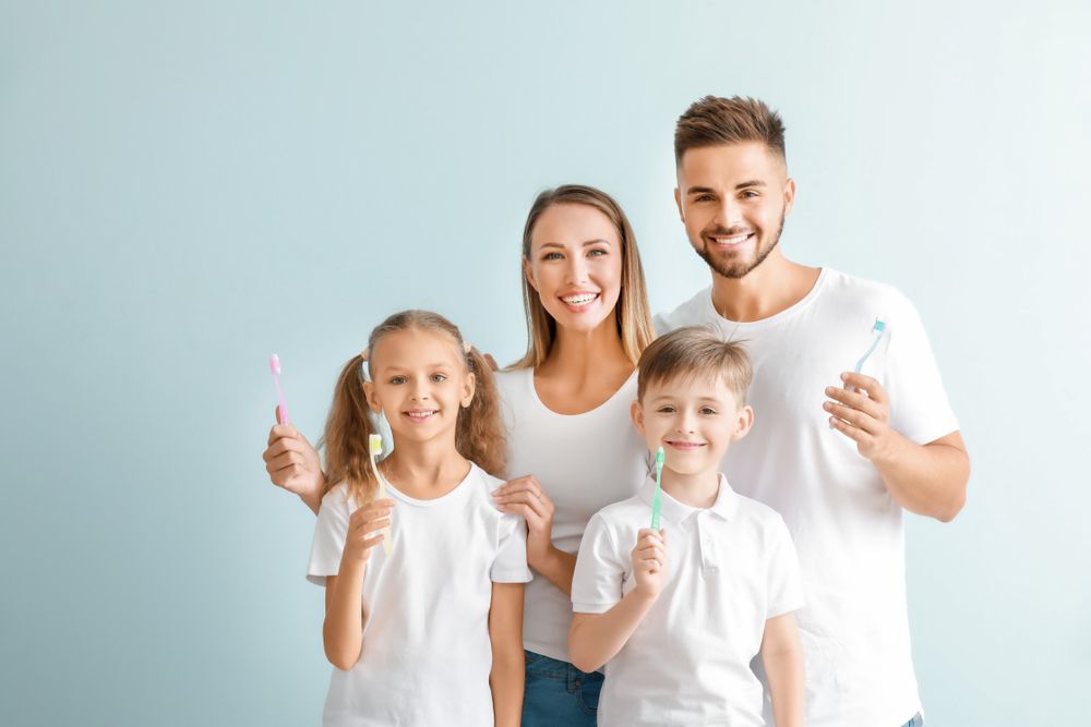 Family smiling with toothbrushes, blue background.