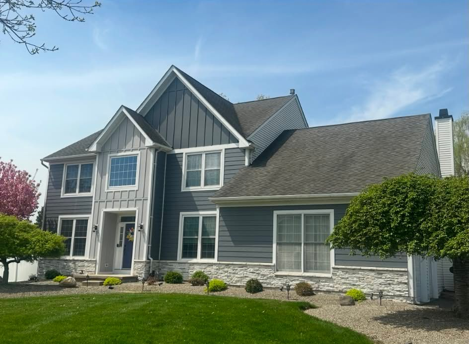 Suburban house with white siding, stone accents, and a curved driveway under sunny trees