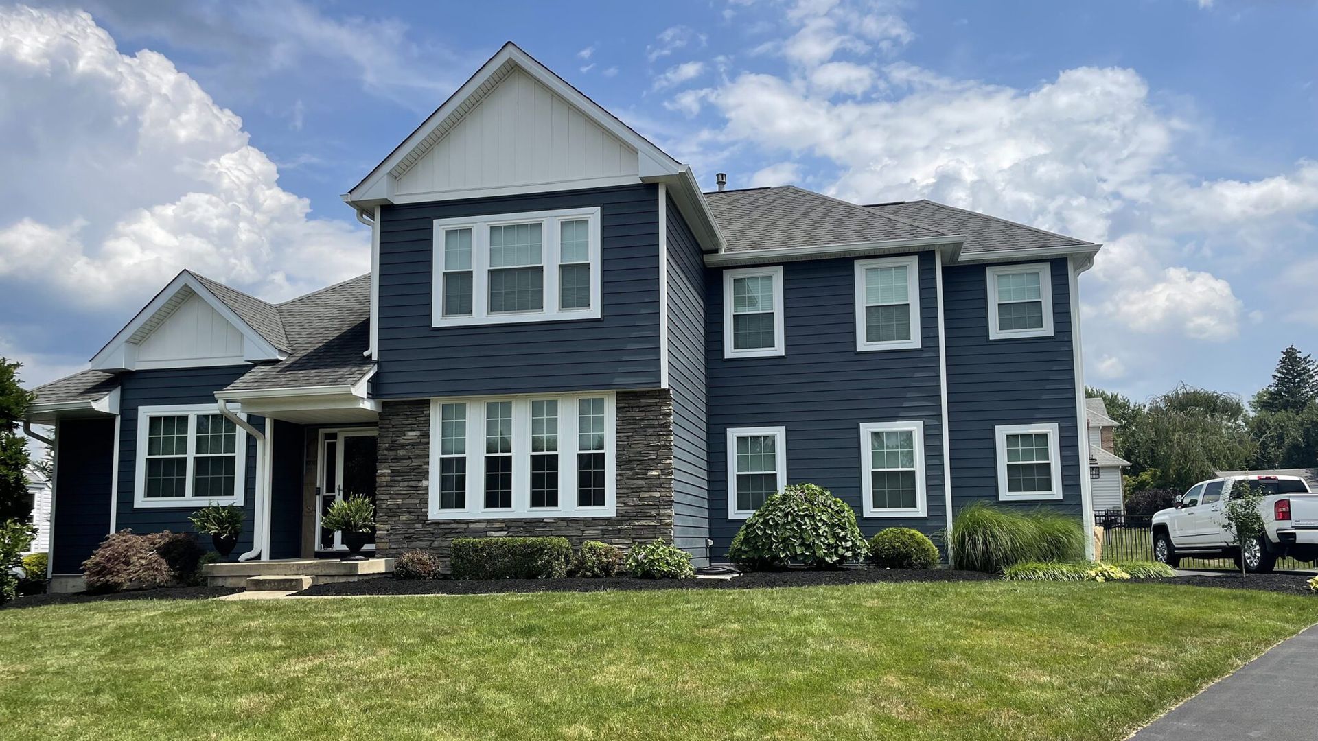 Two-story dark blue suburban house with white trim and stone facade under a cloudy sky