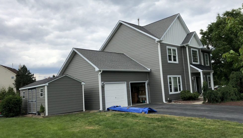 Gray suburban house with attached garage and blue tarp on the driveway under a cloudy sky
