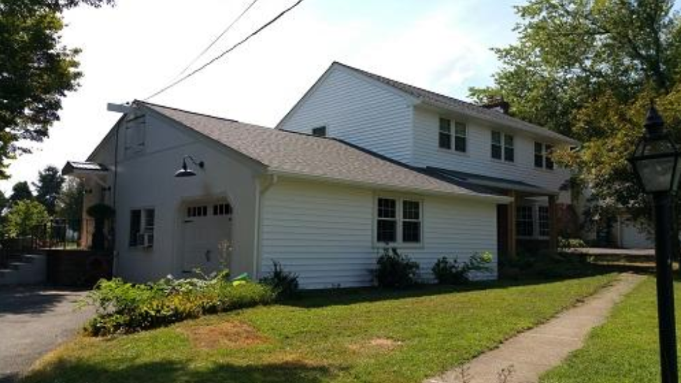 White house with a garage and sloped roof beside a sidewalk on a sunny residential street