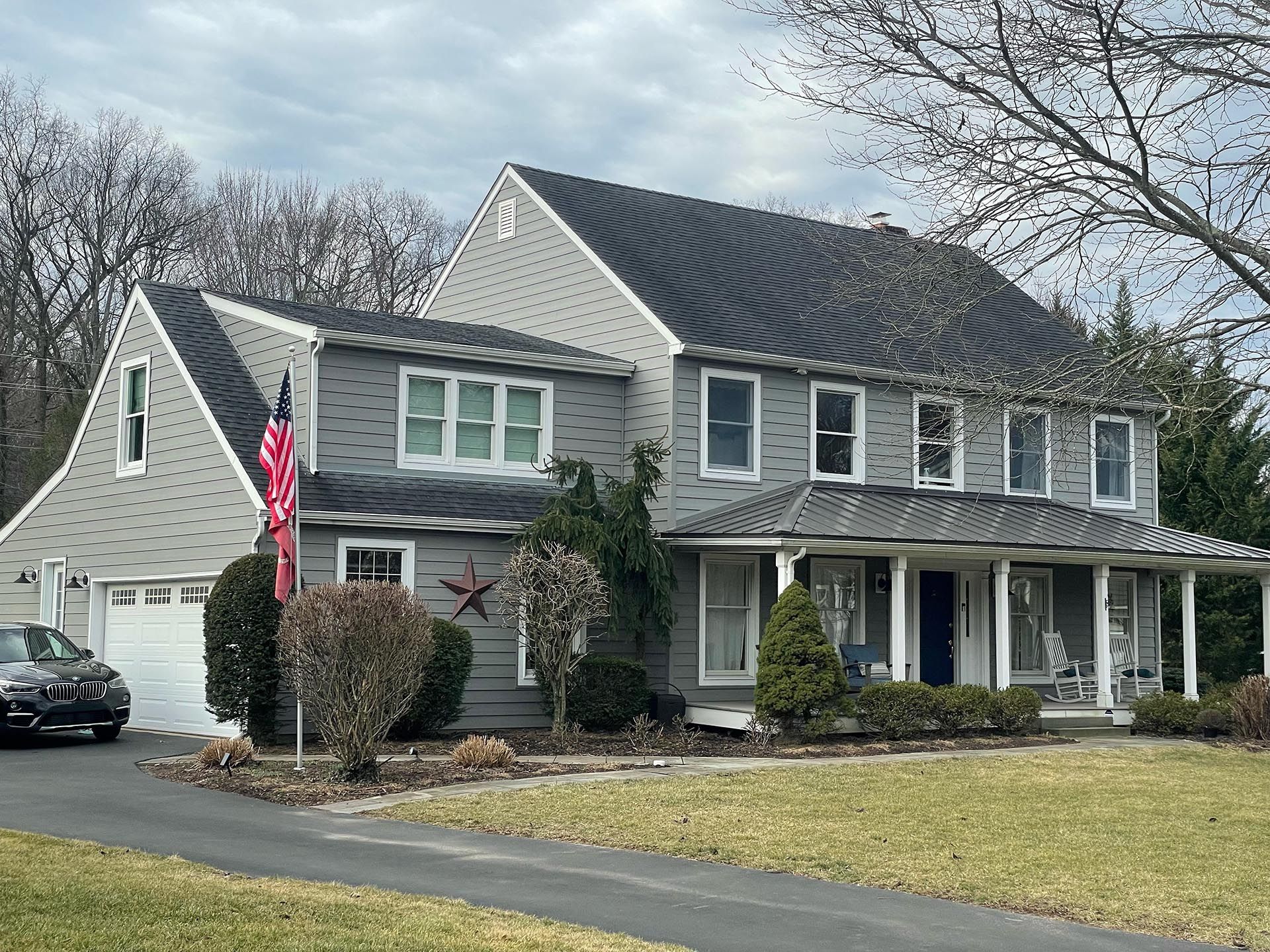 Gray two-story house with an American flag, white porch columns, and a detached garage on a suburban lot