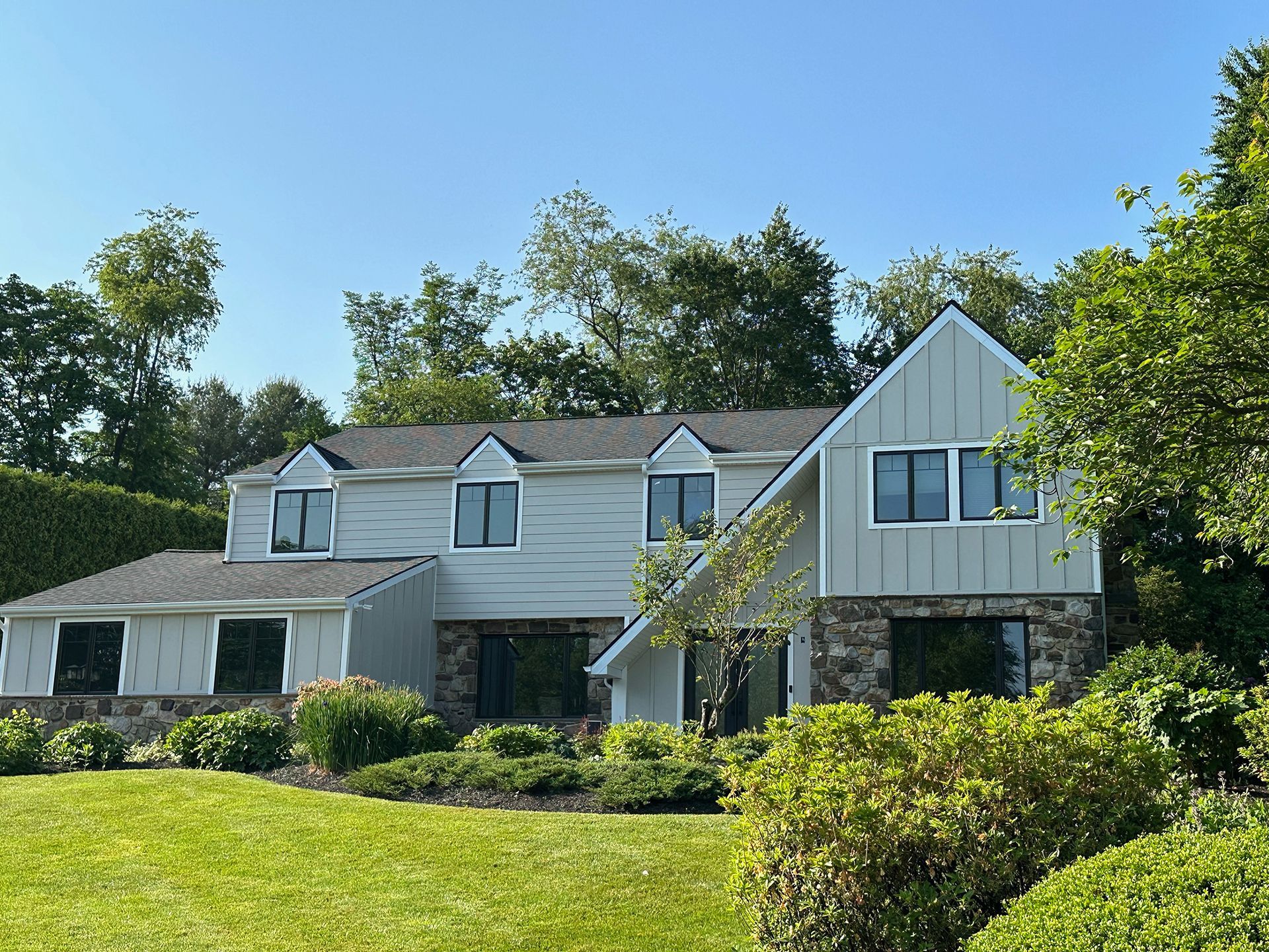Large white house with gray roof, dormer windows, and landscaped lawn under a clear blue sky