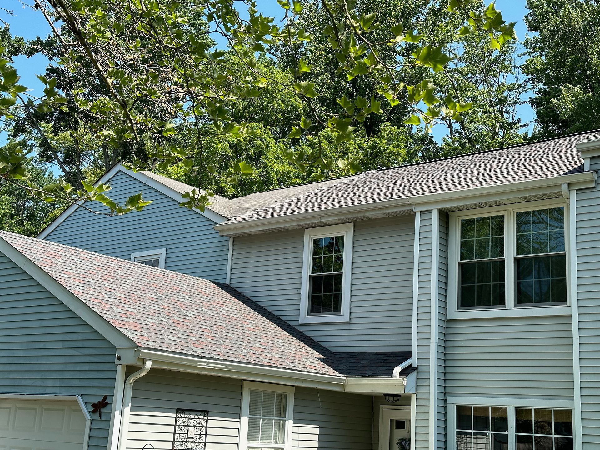 Two-story gray house with white trim and trees overhead