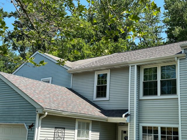 Suburban house with gray siding and white trim under leafy green trees