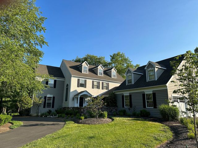 Large cream-colored house with dark roof, dormers, and a landscaped front yard under a blue sky