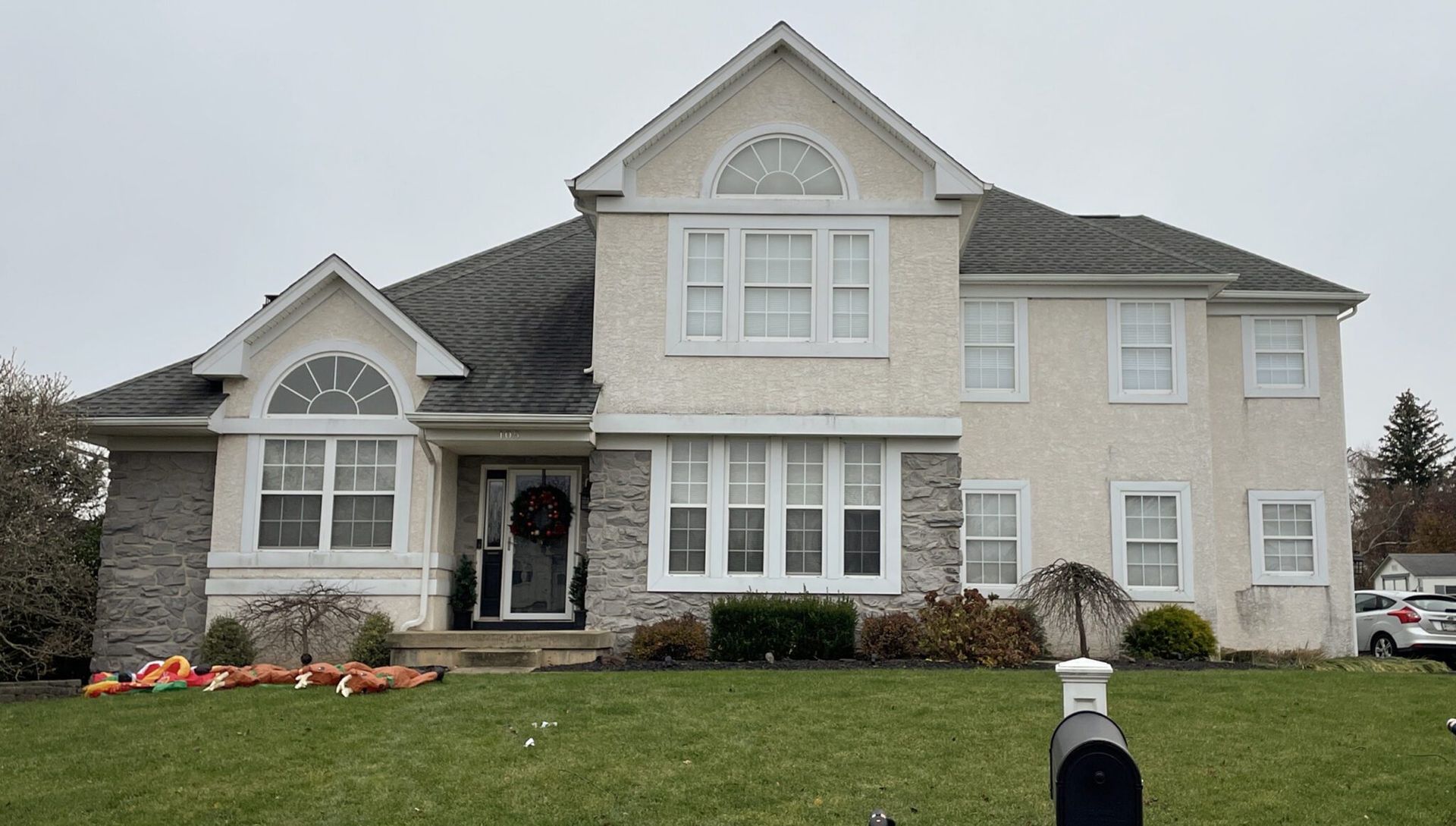Suburban two-story beige house with a manicured lawn and stone accents under an overcast sky