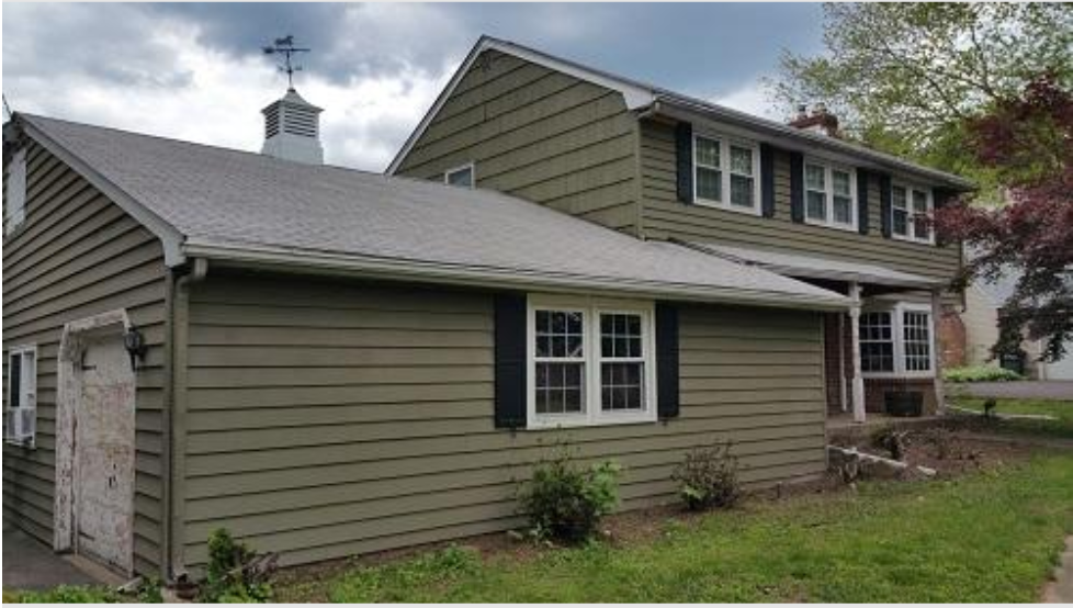 Suburban house with green siding, white trim, and a small front porch under a cloudy sky
