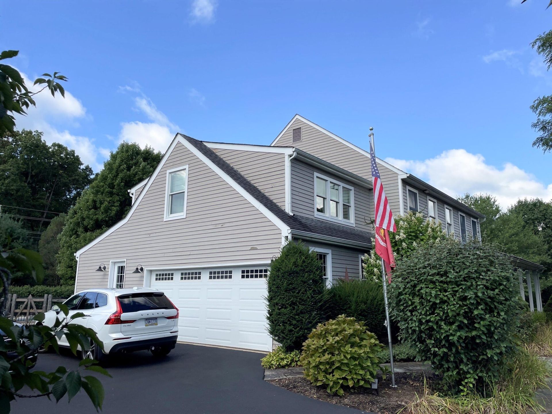 Suburban house with gray siding, white garage, parked car, and an American flag by the front yard.