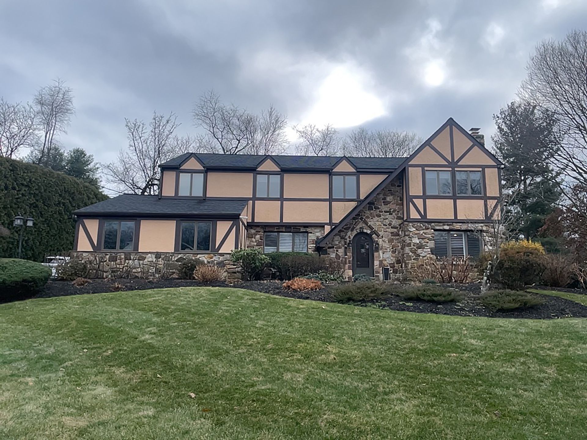 Large Tudor-style house with stone accents on a grassy hill under a cloudy sky
