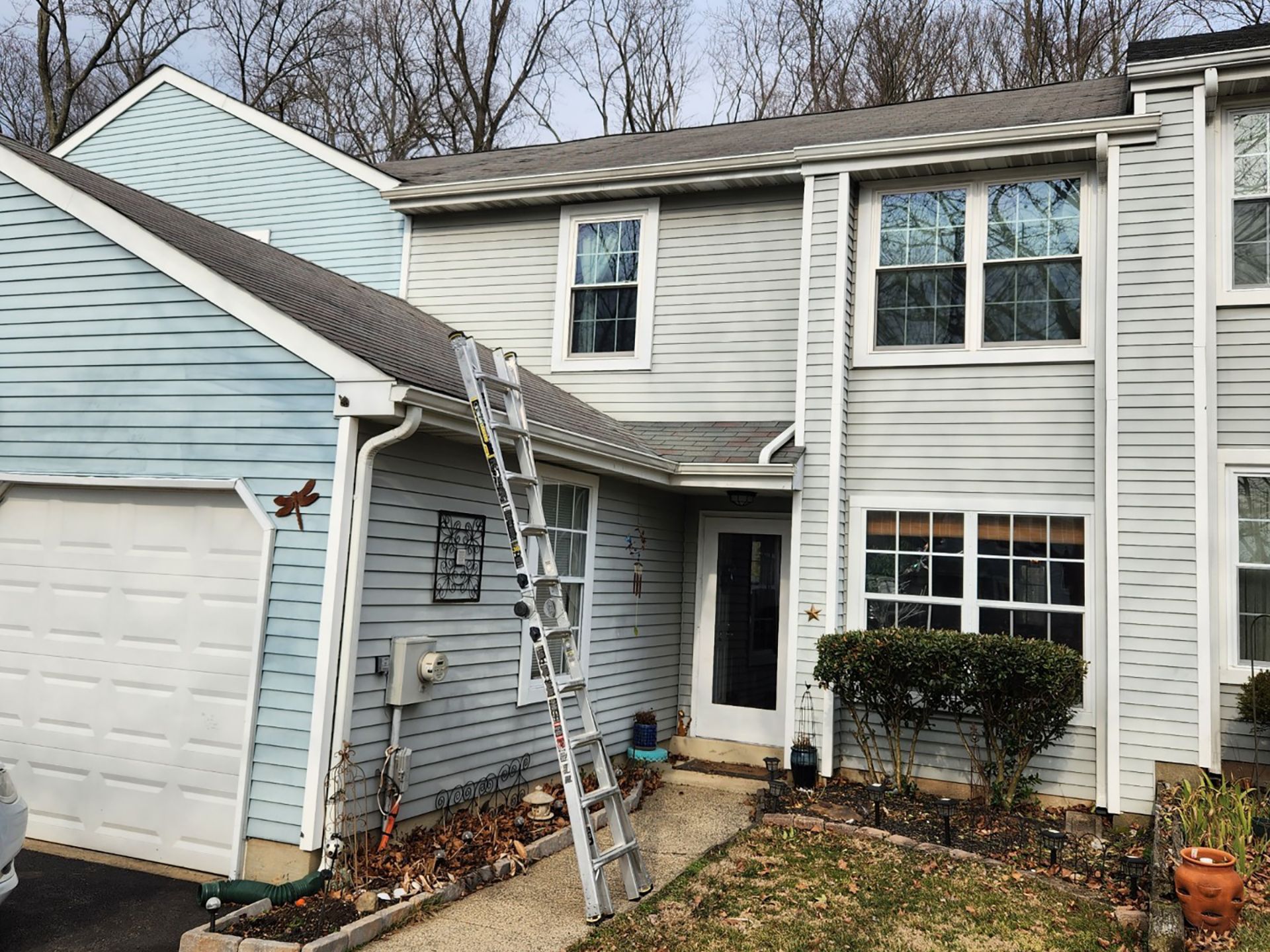 Two-story light blue house with a ladder propped against the front entrance and garage.