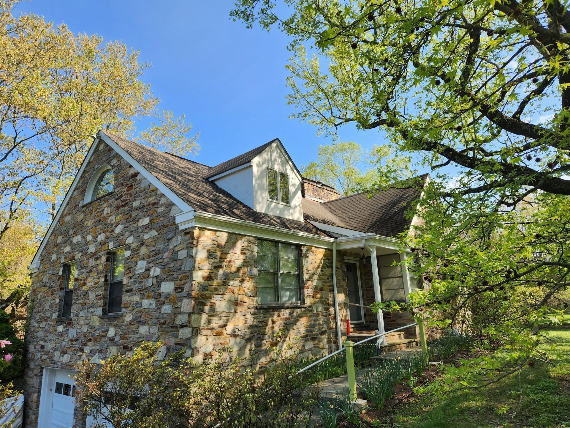 Stone cottage with a steep roof nestled among trees on a sunny hillside