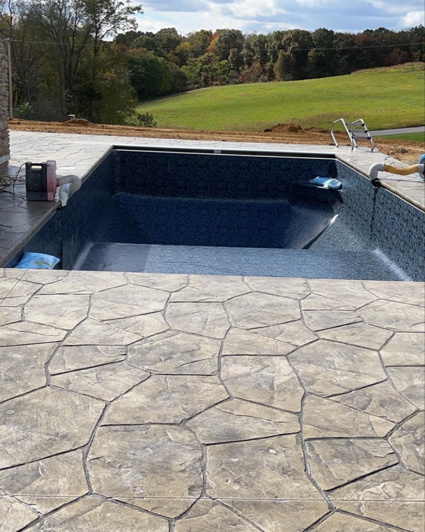 Newly constructed pool with stone patio and grassy background.