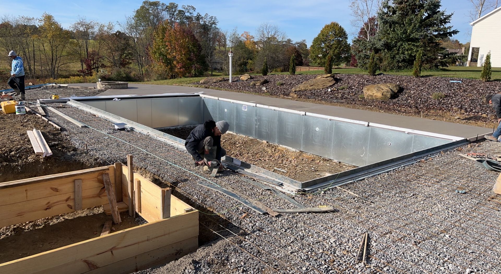 Construction of a rectangular pool. Workers in the pool shell placing gravel. Exterior setting, gravel ground.