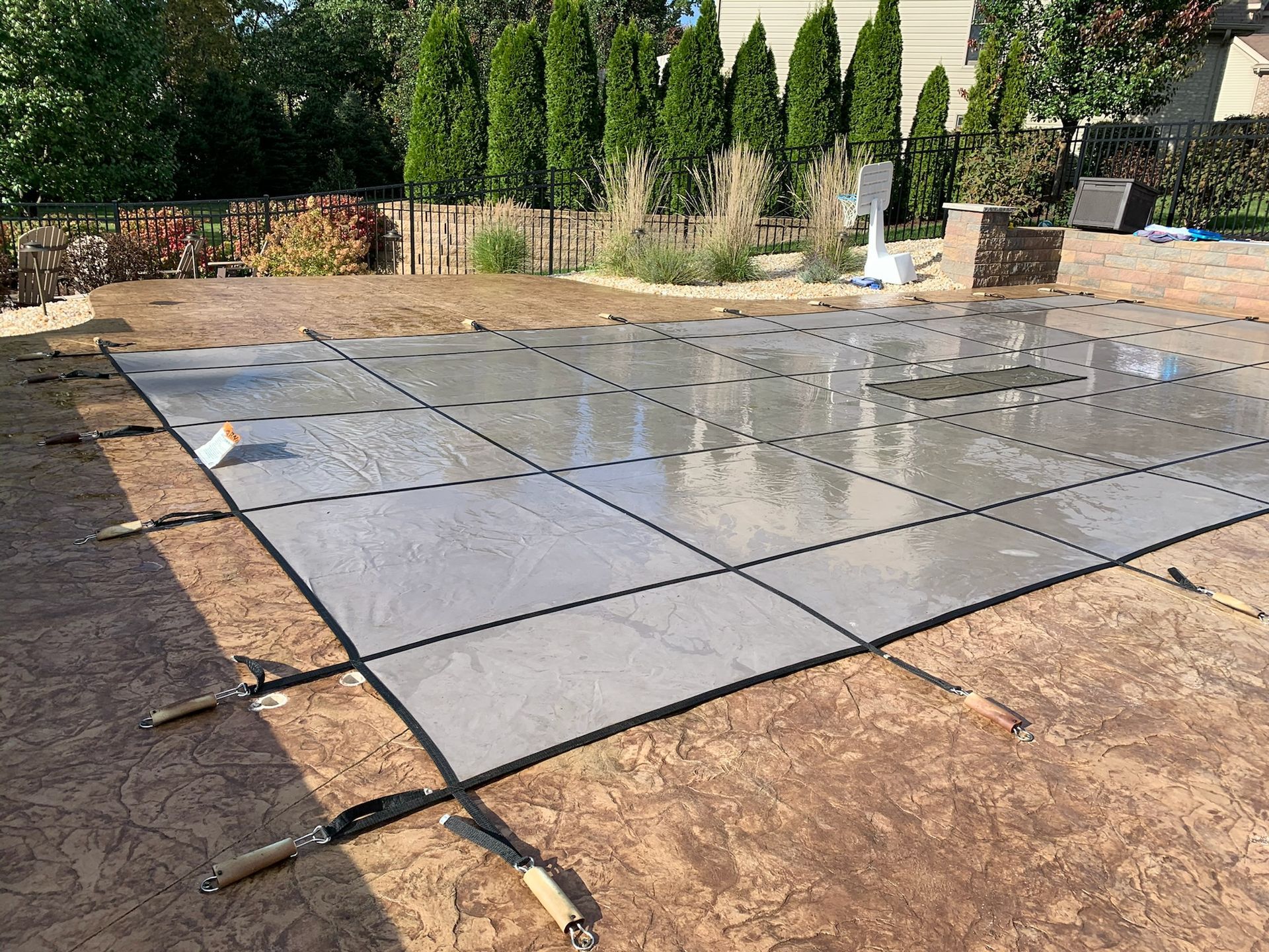 Concrete pool deck under construction, with black grid, trowels, and surrounding brown ground.