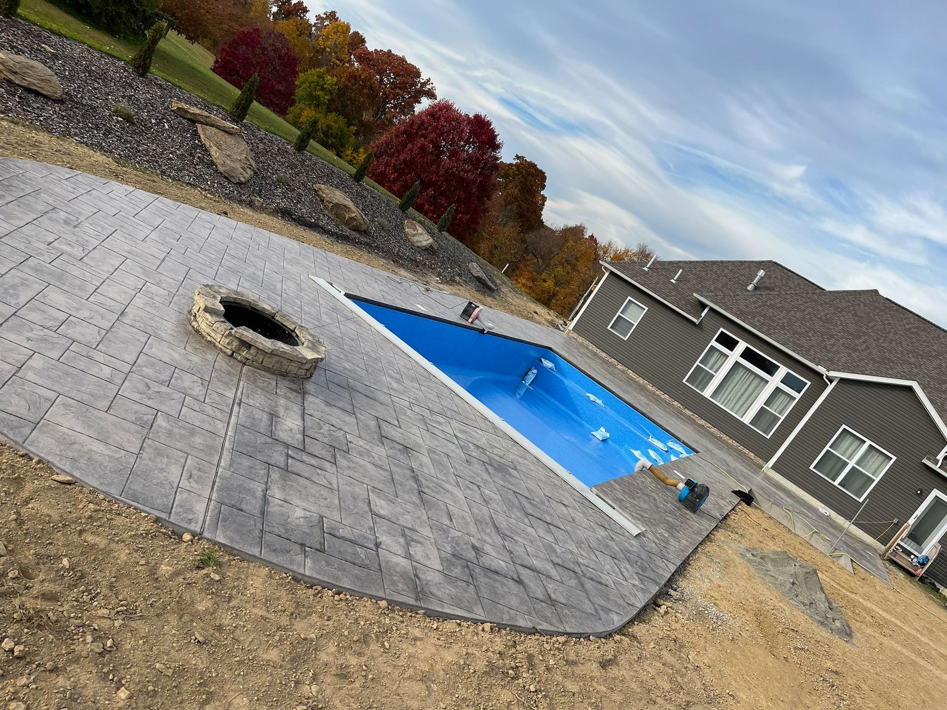 Backyard pool with a blue cover, surrounded by gray paving, next to a house under a cloudy sky.