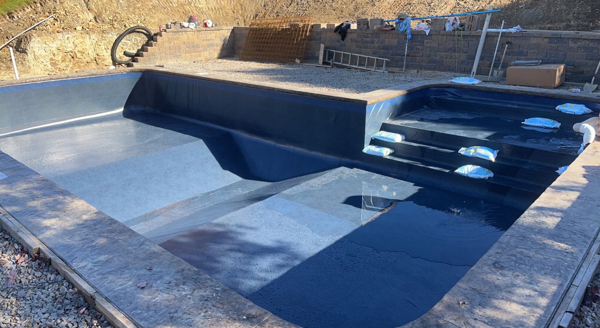 A partially constructed swimming pool with dark blue interior and steps. The setting appears to be outdoors.