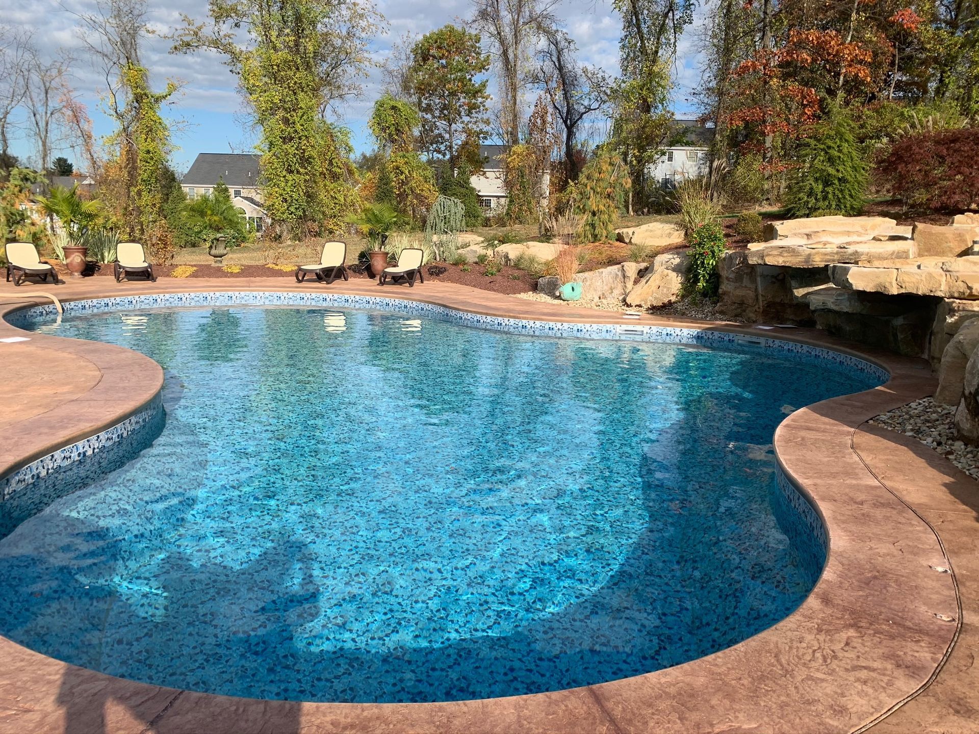 Swimming pool with blue water and stone surround, surrounded by trees.