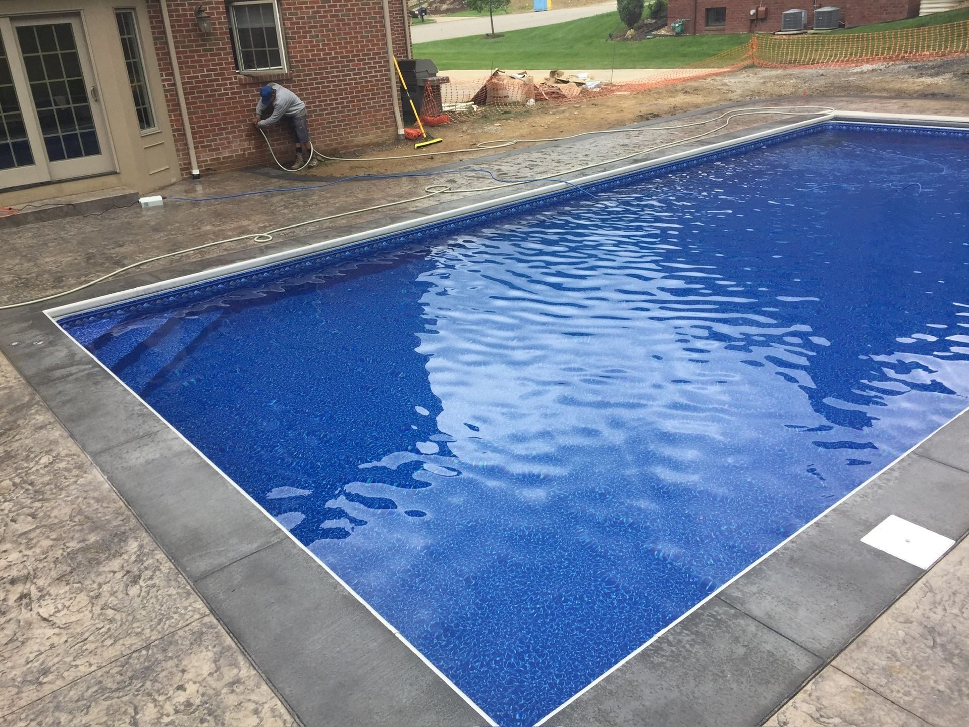 Rectangular pool with blue water and gray concrete surround. Man working nearby.