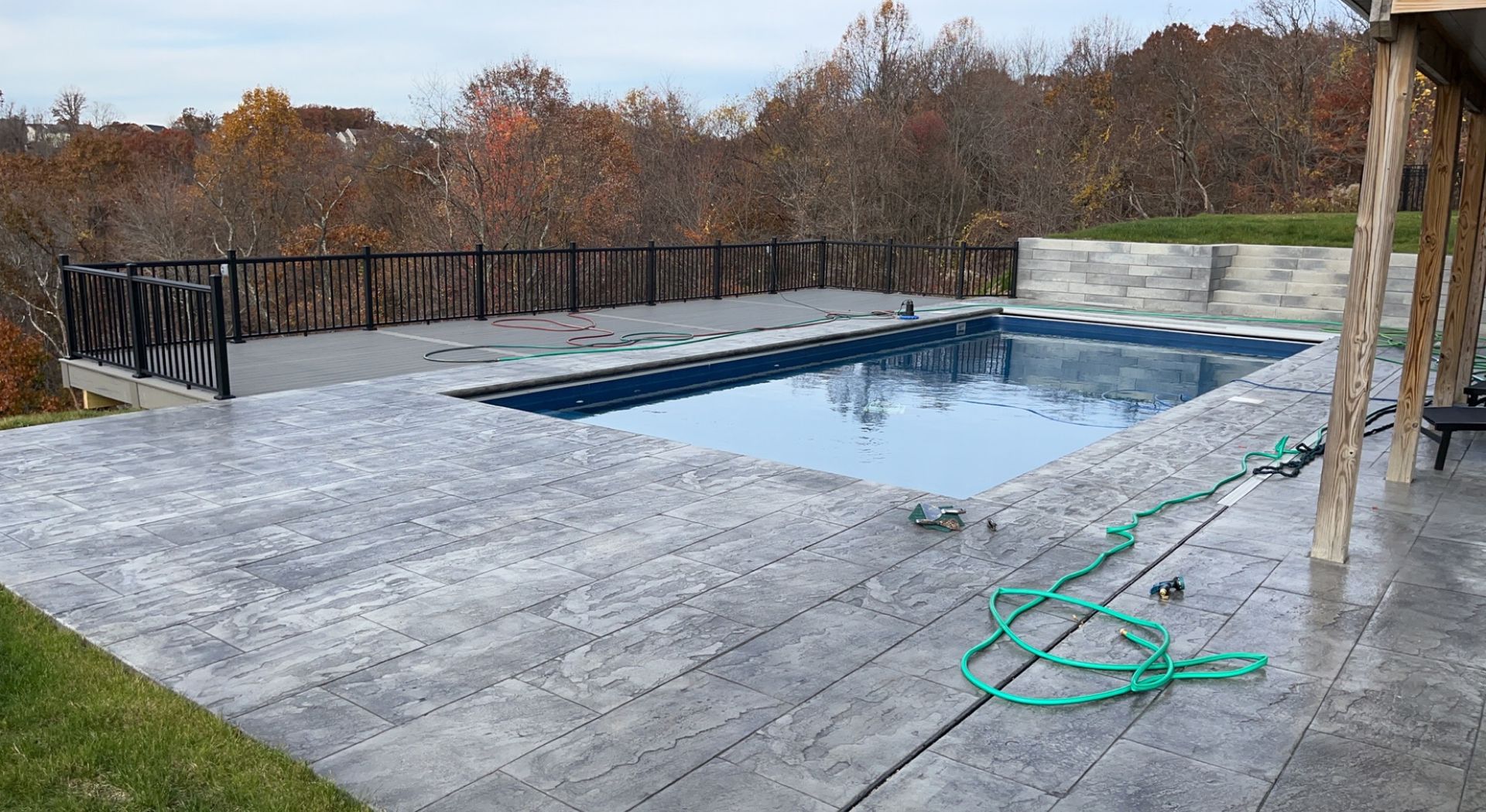 Pool area with gray concrete patio and black railing overlooking fall foliage.
