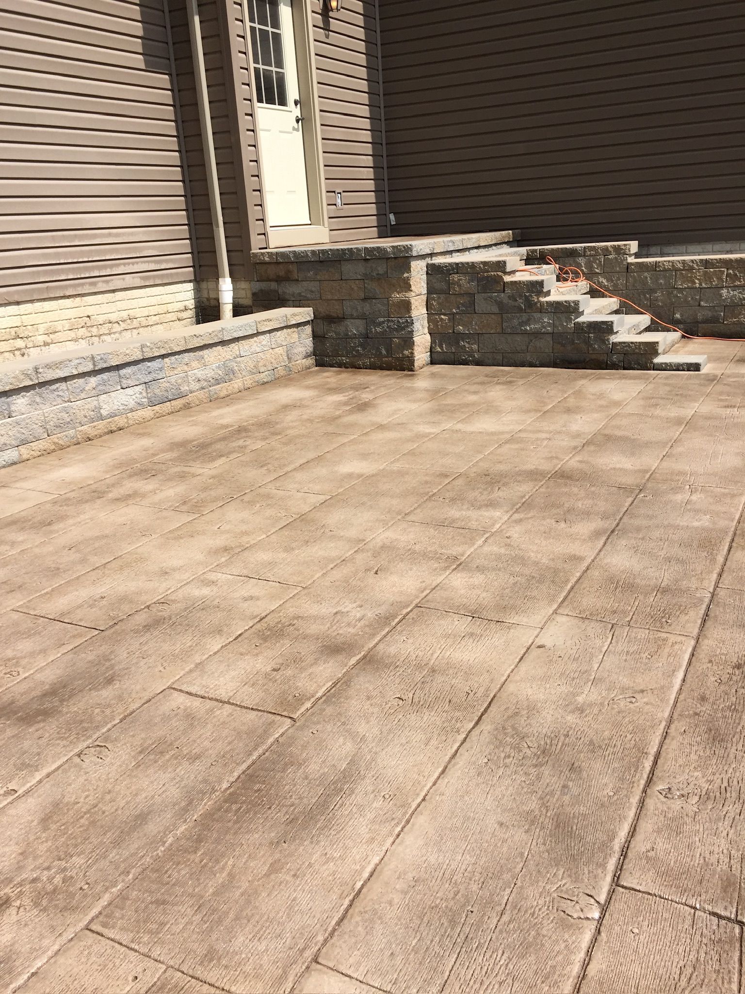 Brown patio with brick steps leading to a door; siding background.