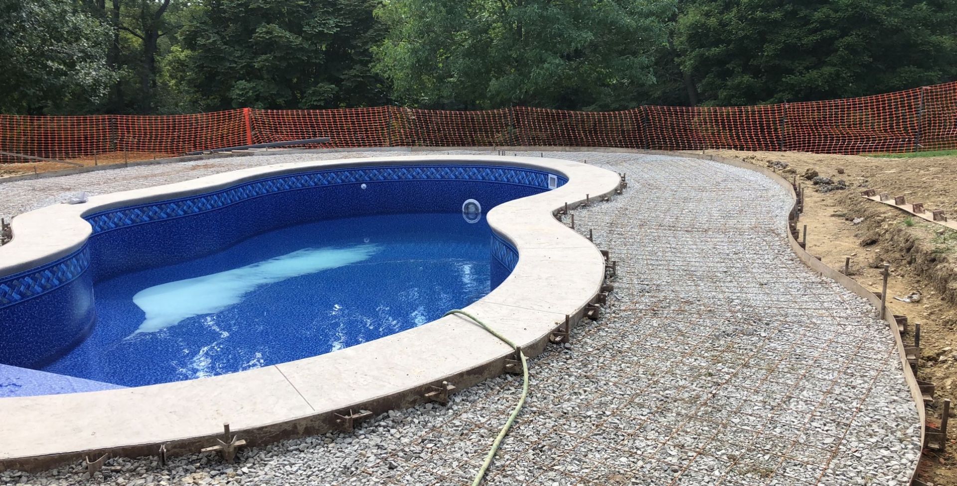 Pool with blue water and textured concrete edging; orange barrier in background.