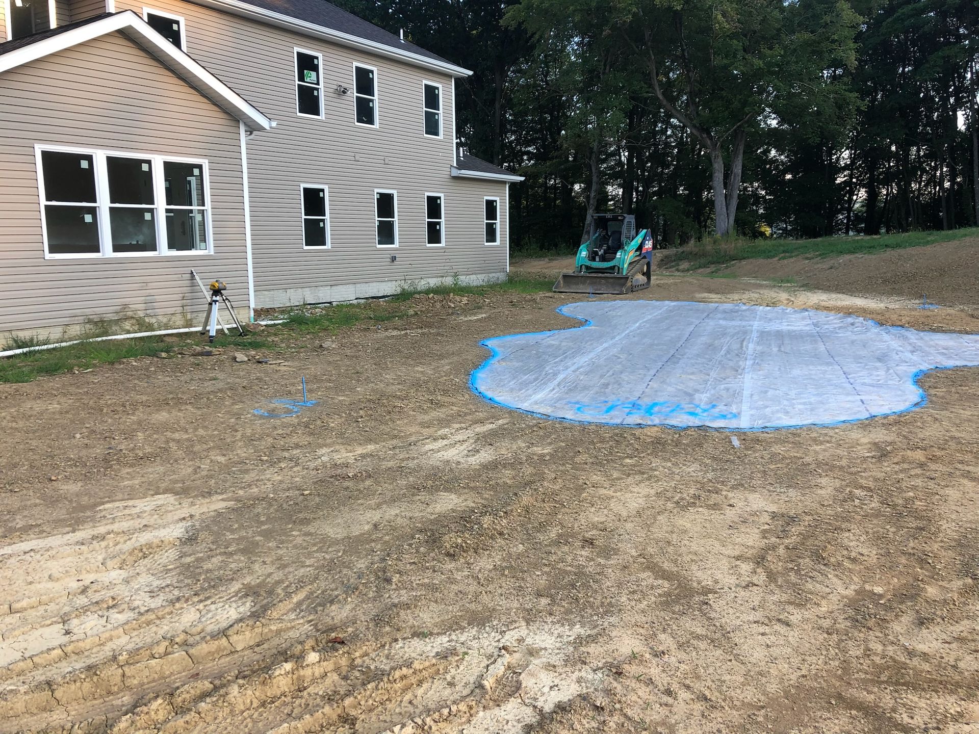 Construction site: house and prepared area outlined in blue for a pool, surrounded by dirt and a small tractor.