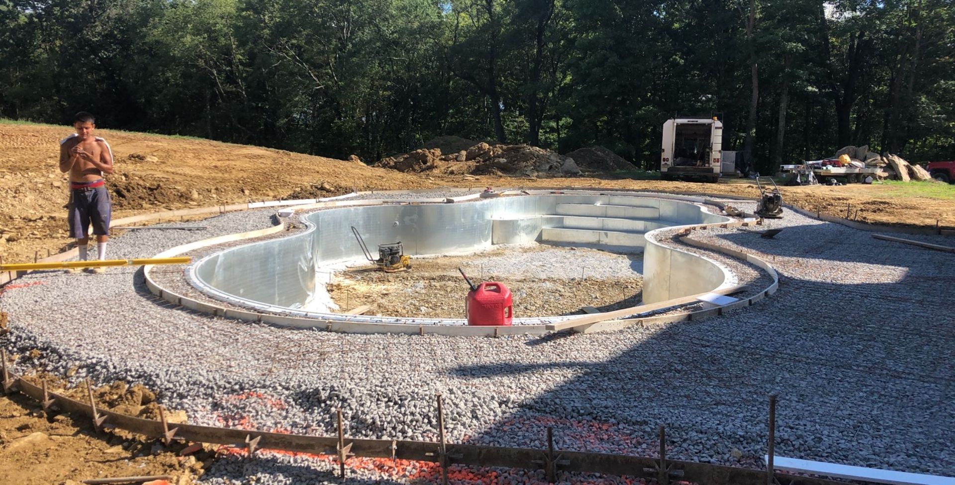 Pool construction: Man standing near a partially built pool with gray gravel surrounding the concrete shell.