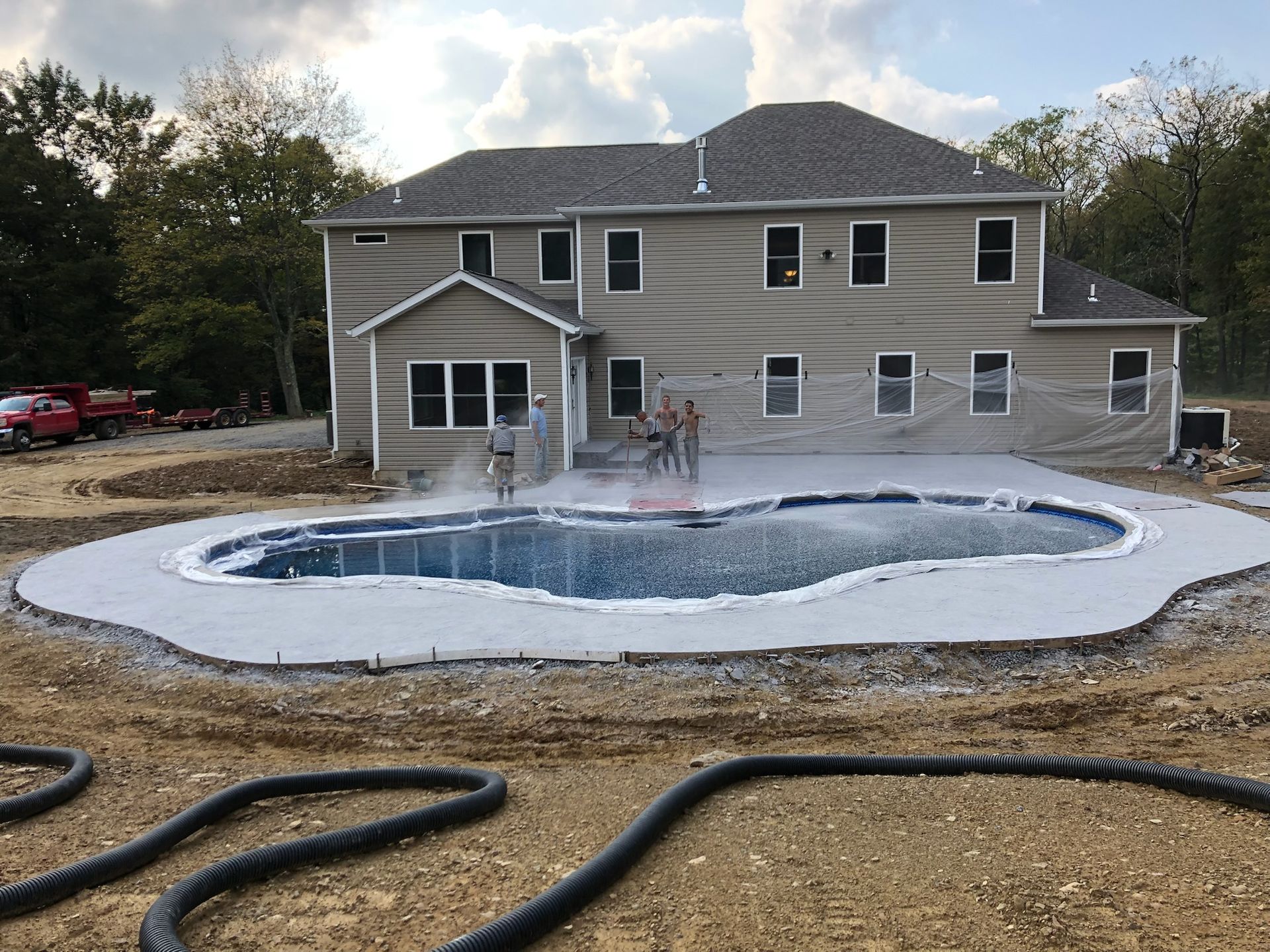 Backyard with a newly constructed pool and house. People stand near the pool.