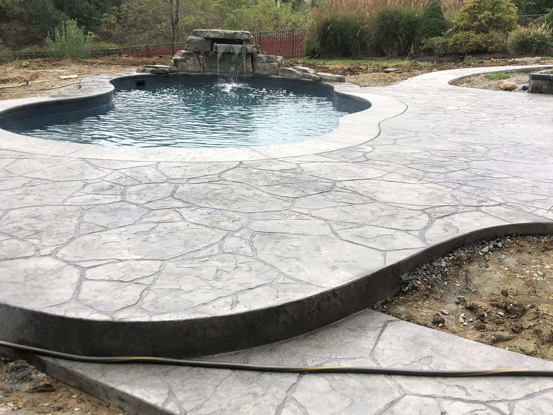 Pool with waterfall feature surrounded by patterned gray concrete patio.