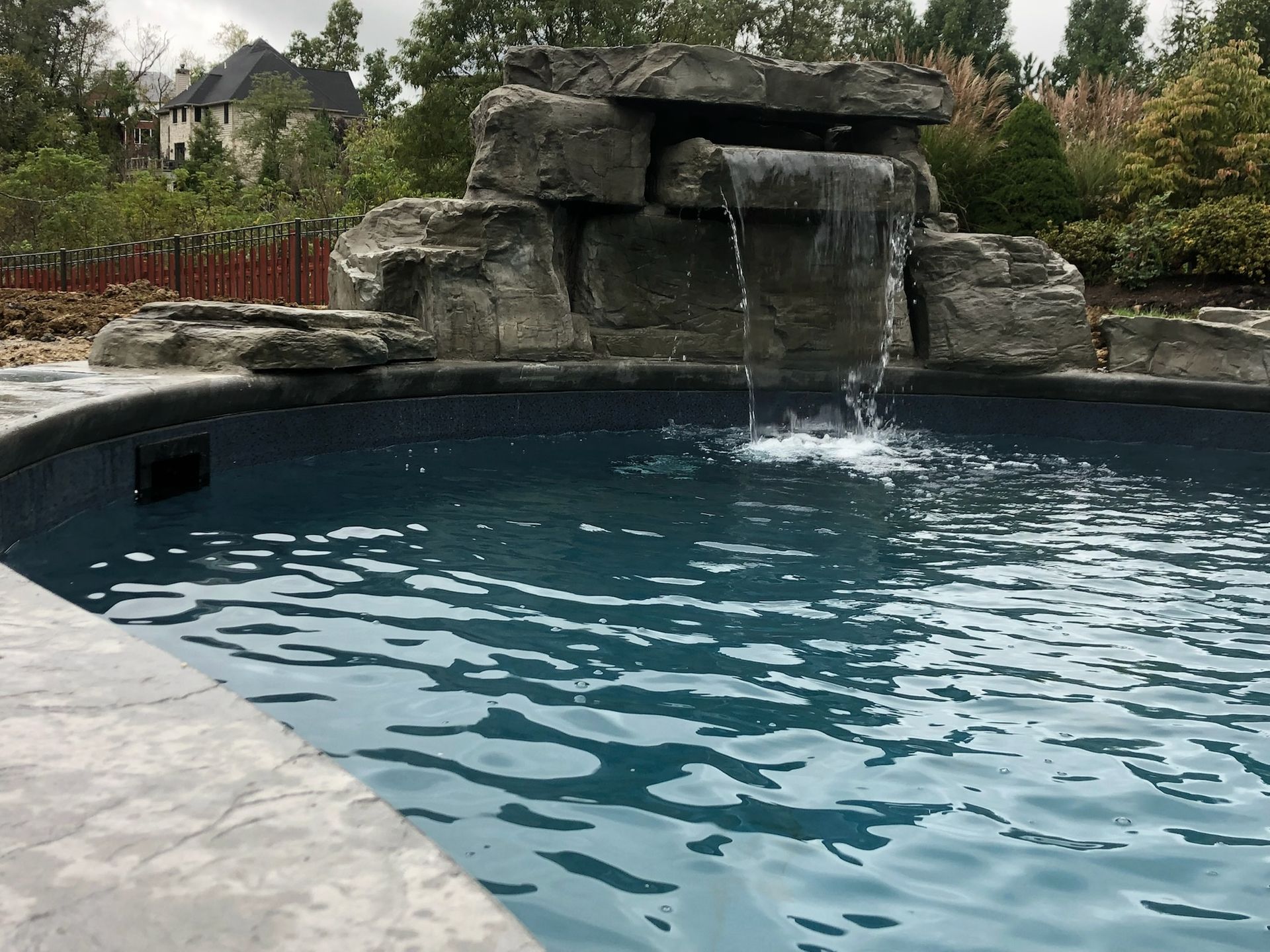 Waterfall cascading into a dark blue swimming pool; gray stone structure in the background.