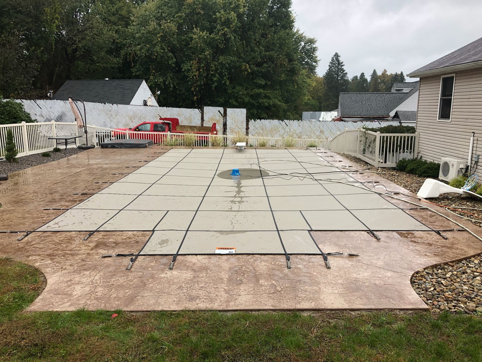 Concrete pool deck under construction with exposed rebar, in a residential yard.