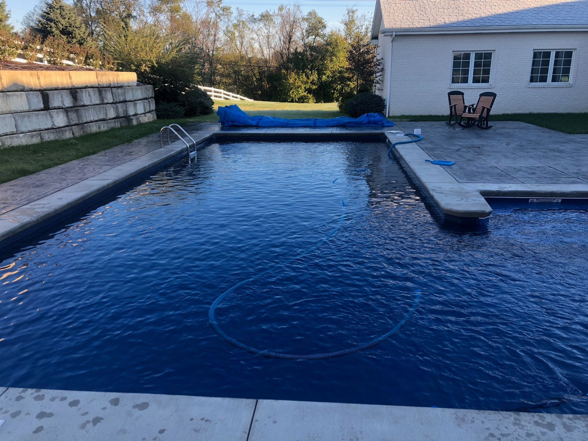 A rectangular swimming pool filled with dark blue water.  A blue cover lies on one section, with a concrete deck surrounding it.