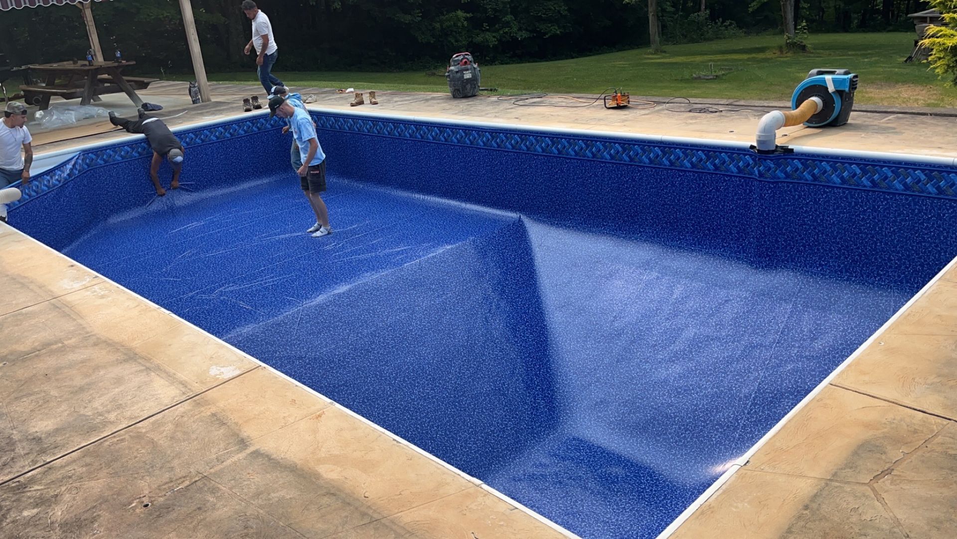 People installing blue patterned pool liner in a rectangular pool.