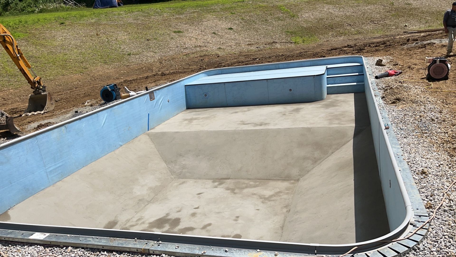 Newly constructed swimming pool with blue interior and concrete steps. An excavator is visible.